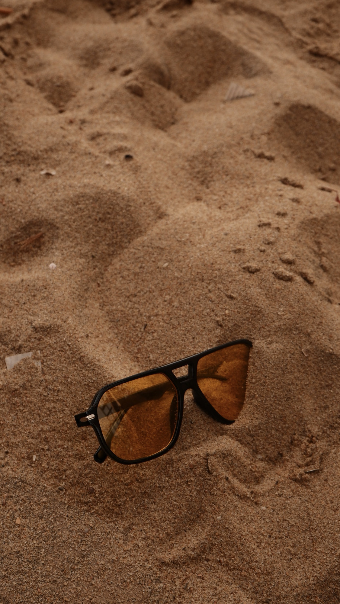 Amber sunglasses half buried in sand