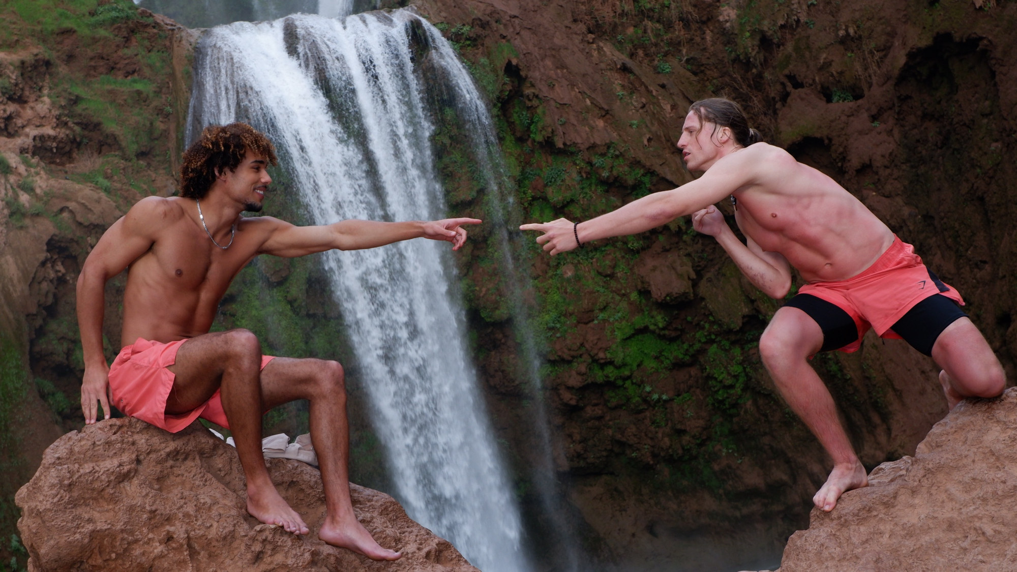 João and a friend pointing at each other in front of a waterfall